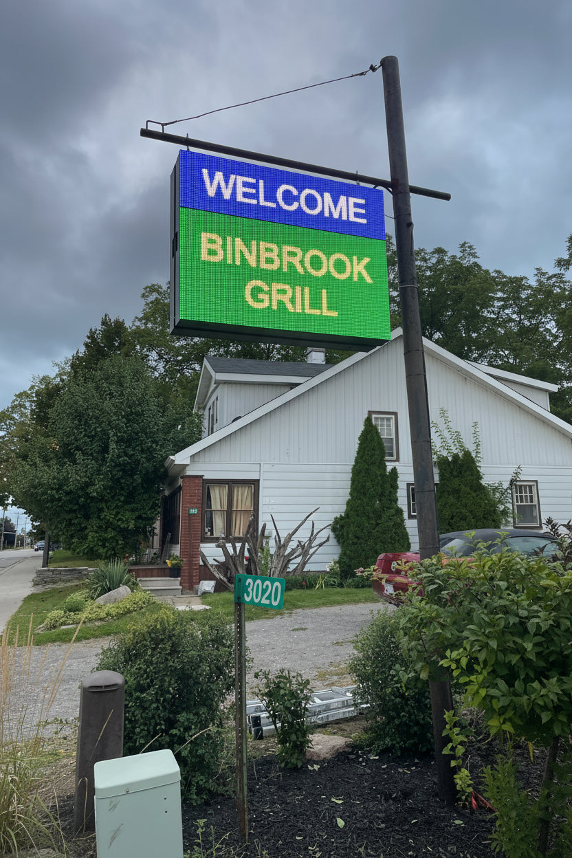 Outdoor LED sign displaying 'WELCOME BINBROOK GRILL' in blue and green colors mounted on a post.