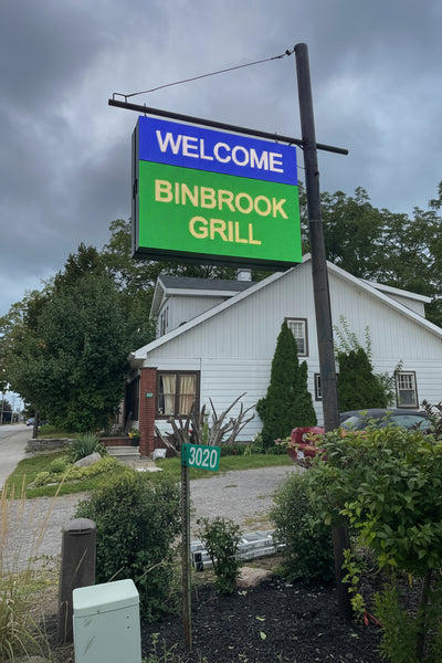 Outdoor LED sign displaying 'WELCOME BINBROOK GRILL' in blue and green colors mounted on a post.