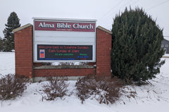 Outdoor LED sign for Alma Bible Church, displaying text in colorful letters against a nighttime backdrop.